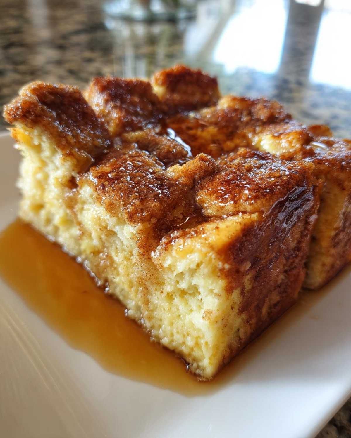 A close-up of a moist slice of baked french toast topped with cinnamon sugar and drizzled with syrup.