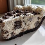 A close-up of a delicious slice of cookies and cream ice cream pie with chocolate crust and whipped cream.
