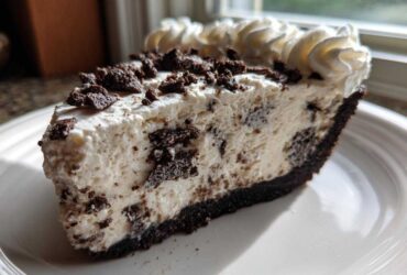 A close-up of a delicious slice of cookies and cream ice cream pie with chocolate crust and whipped cream.