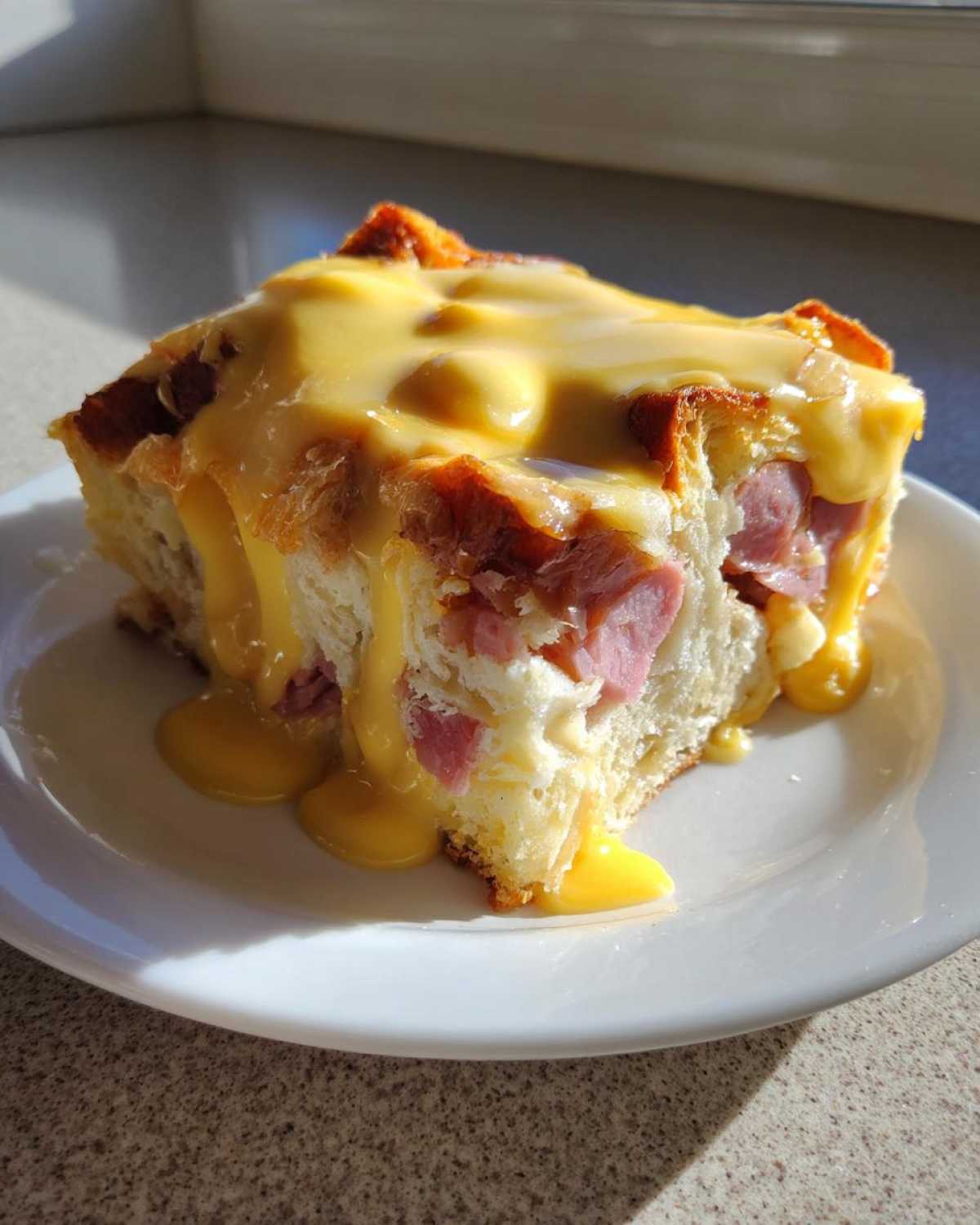 A single serving slice of eggs benedict casserole topped generously with dripping hollandaise sauce.