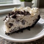 A generous slice of cookies and cream ice cream pie with a dark crust, creamy filling, and whipped topping.