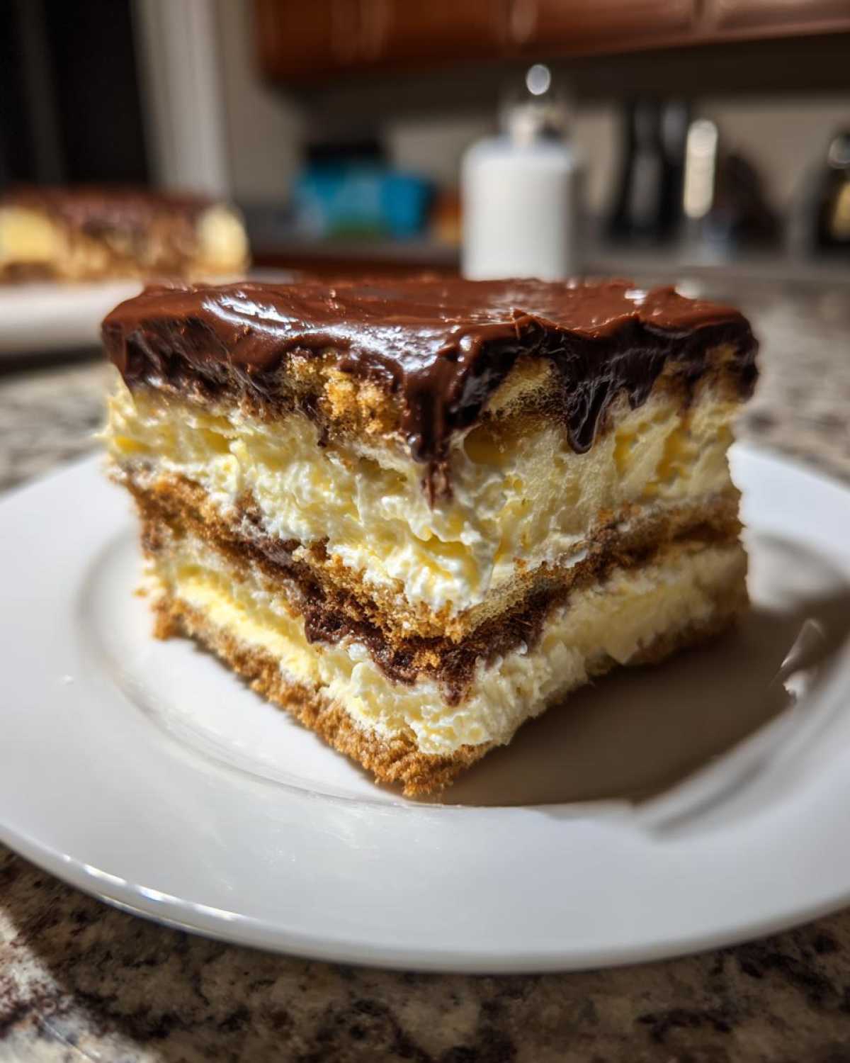 A close-up slice of layered eclair cake with creamy filling and chocolate frosting.