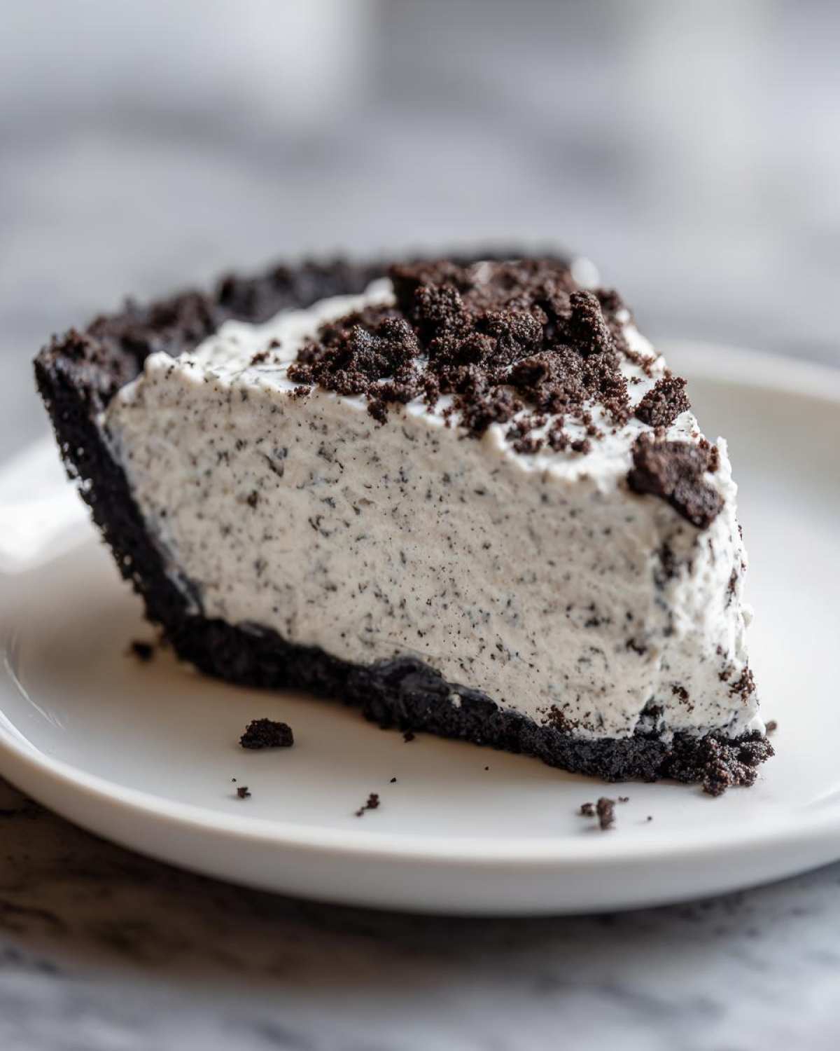 Close-up of a creamy slice of oreo pie with a dark chocolate crust and cookie crumble topping.