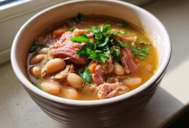 A close-up of a bowl of rich bean soup topped with shredded ham and fresh parsley.