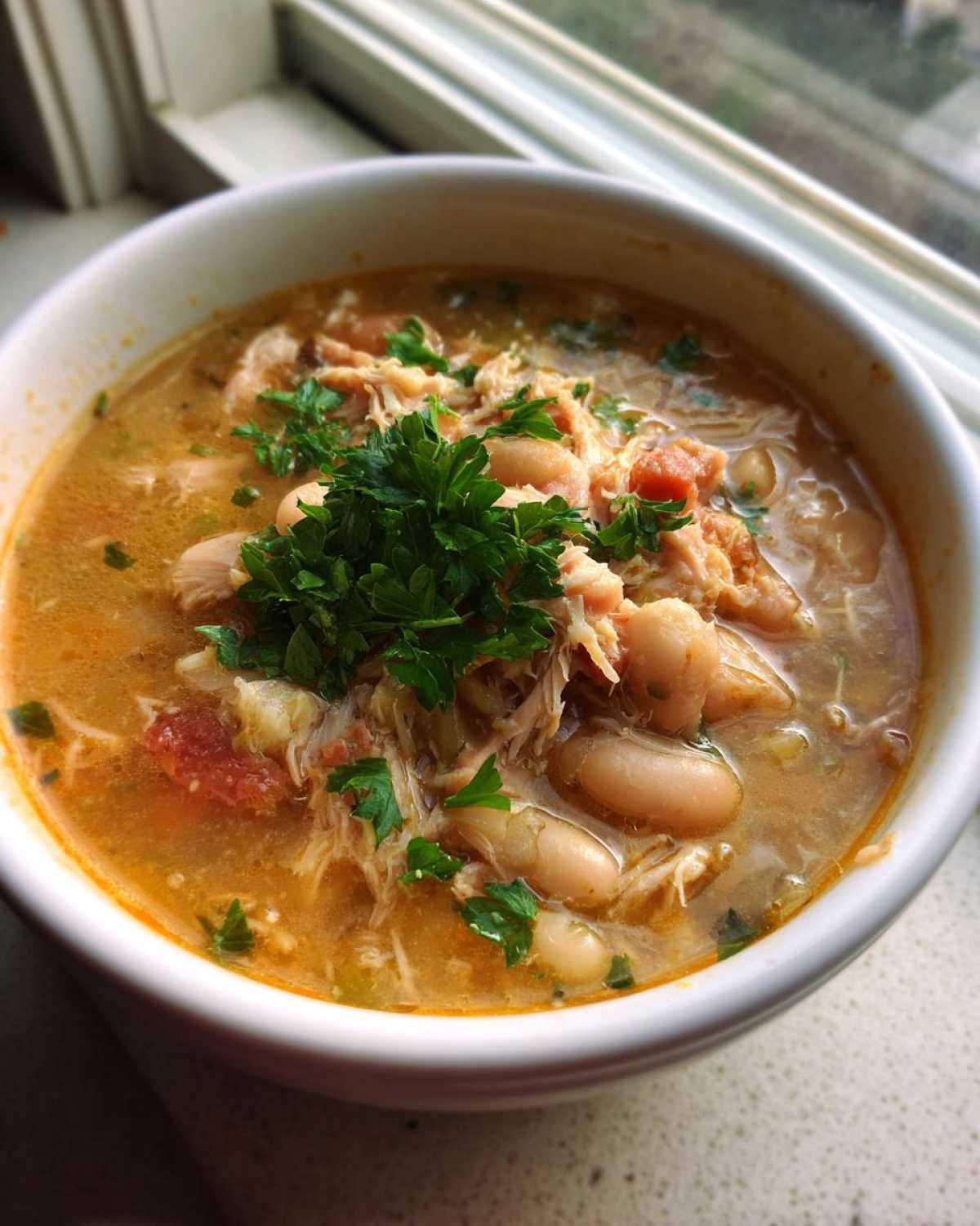 Close-up of a bowl of hearty chicken and white bean soup, garnished with fresh parsley.