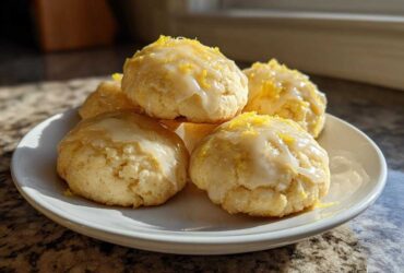A stack of soft italian ricotta cookies topped with a white lemon glaze and bright yellow zest.