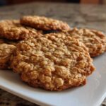 Close-up of several soft oatmeal cookies piled on a white rectangular plate.