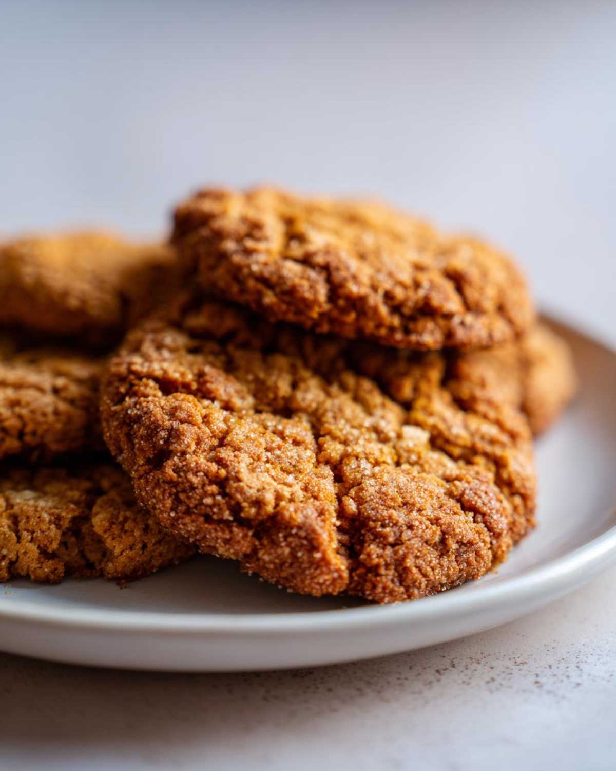 Close-up of a stack of soft, chewy, sugar-coated oatmeal cookies on a light plate.