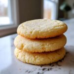 Close-up of three soft sugar cookies stacked on a marble counter, lightly sprinkled with sugar.
