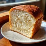 A close-up of a freshly baked loaf of sourdough sandwich bread, showing its soft, white interior crumb.