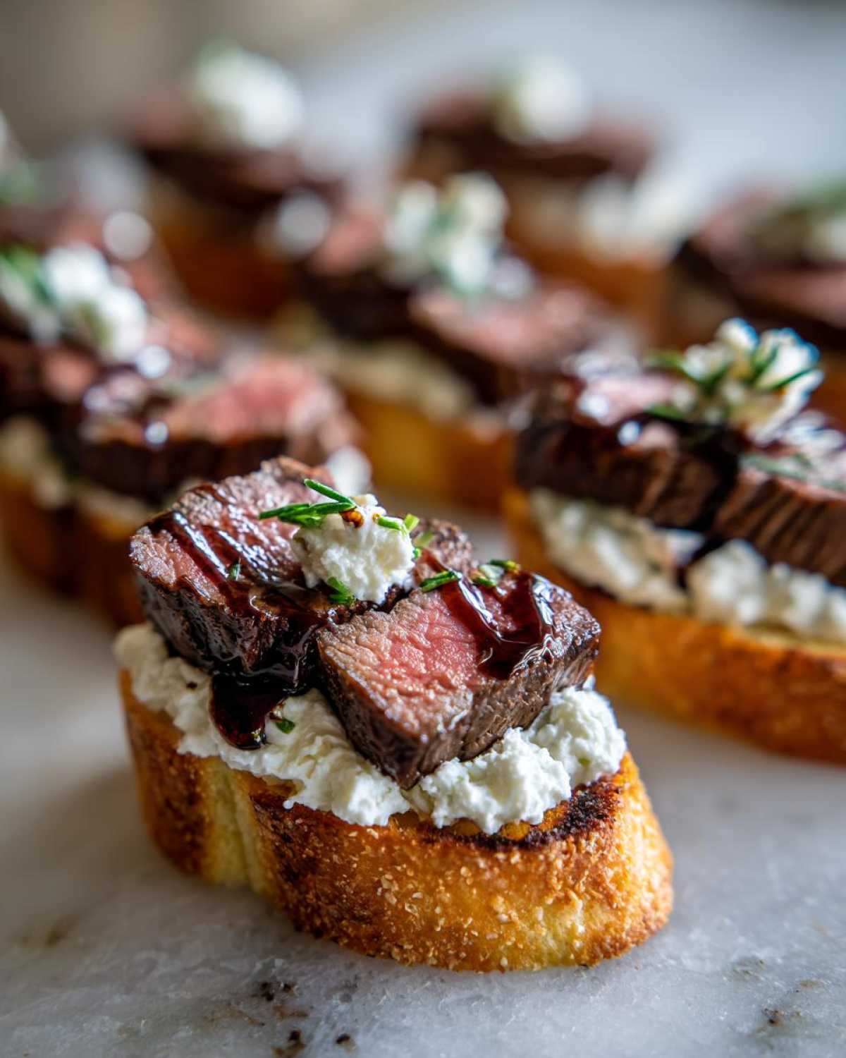 Close-up of a single steak crostini topped with rare steak, creamy cheese, and a balsamic drizzle.