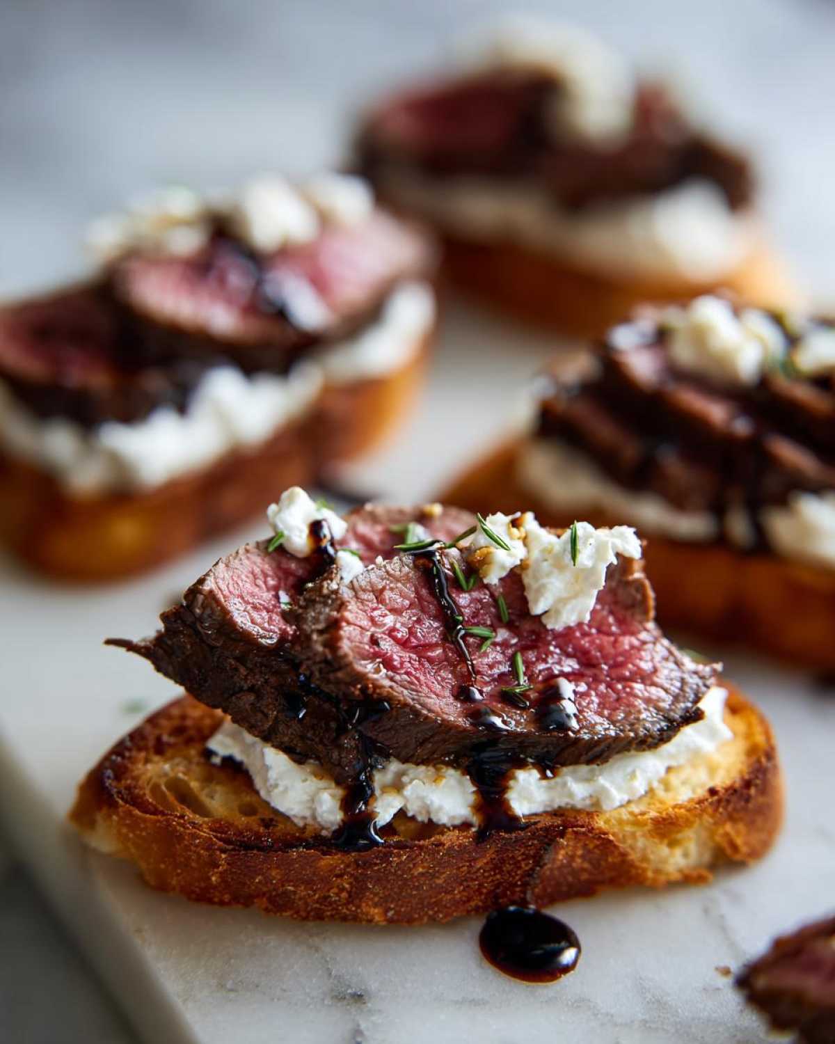 Close-up of a steak crostini topped with rare steak, goat cheese, and balsamic glaze.