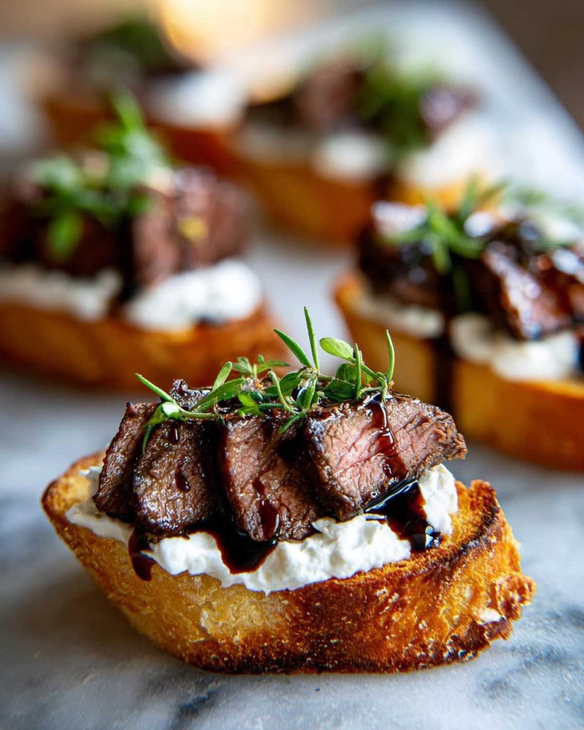 Close-up of a single steak crostini topped with sliced steak, creamy cheese, and fresh herbs.