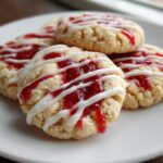 Close-up of several delicious strawberry cheesecake cookies topped with red jam and white icing drizzle.