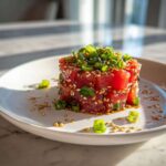 A beautifully molded tower of vibrant red tuna tartare, garnished generously with sesame seeds and sliced green onions.
