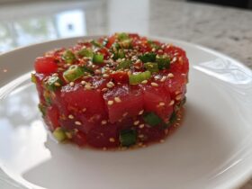 A close-up of a perfectly molded tower of vibrant red tuna tartare, topped with green onions and sesame seeds.