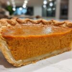 Close-up of a thick slice of sweet potato pie showing the rich orange filling and flaky golden crust.