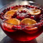 Close-up of a festive thanksgiving punch in a glass bowl garnished with bright orange slices and fresh cranberries.