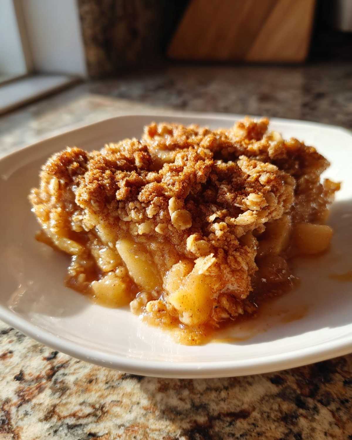 A warm serving of apple crisp recipe with a thick, golden-brown oat topping on a white plate.