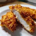 Close-up of air fryer chicken tenders, one piece cut open showing juicy white meat inside a crispy golden breading.