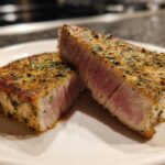 Two halves of a perfectly seared air fryer Tuna steak, showing a medium-rare pink center and herb crust.