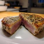 Close-up of a perfectly cooked air fryer Tuna steak, seasoned and seared, cut in half showing a medium-rare pink center.