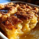 A close-up, sunlit view of a rich, golden brown apple cobbler with a sugary crust, showing the soft filling inside.
