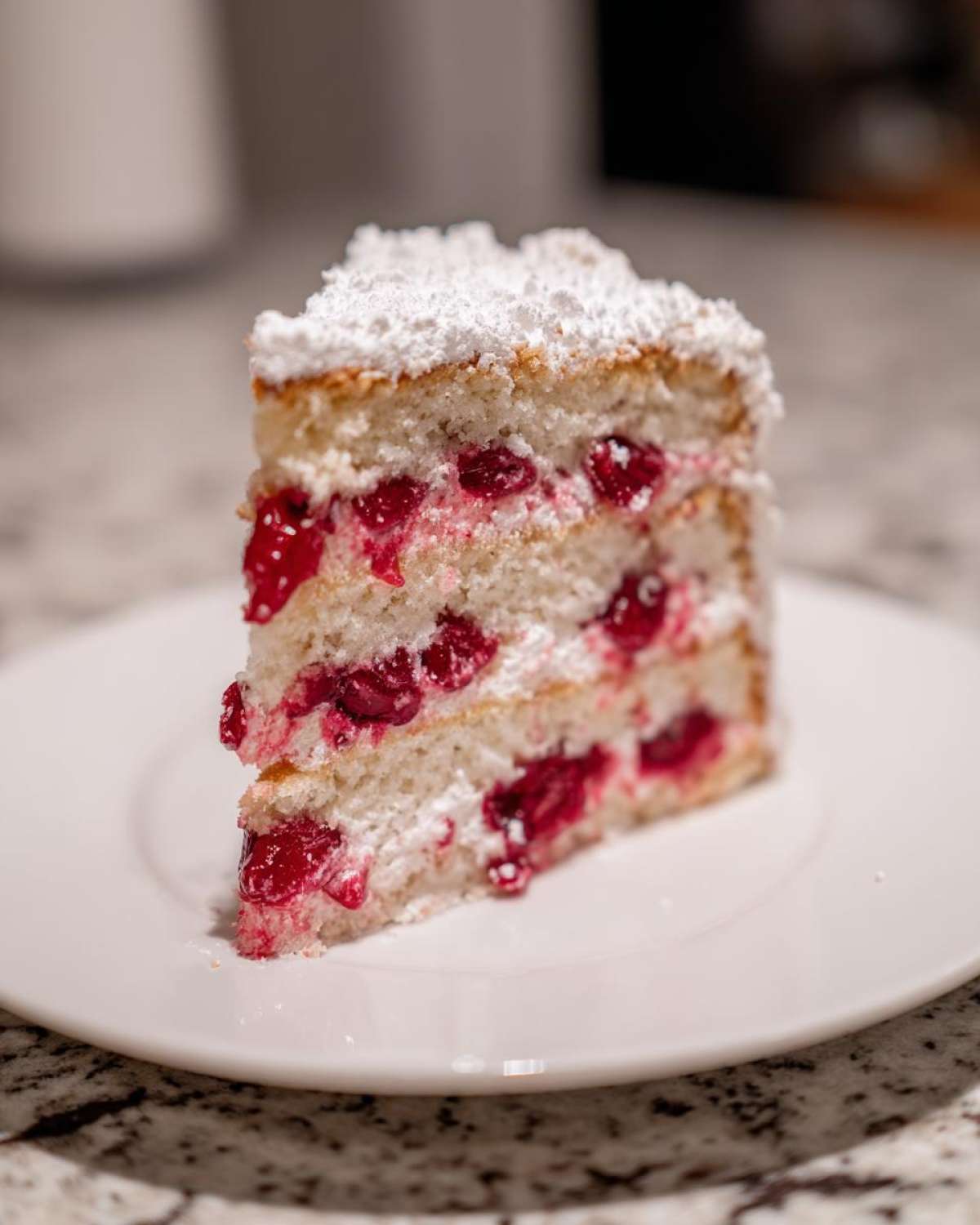A tempting slice of layered cherry cake, filled with bright red cherries and topped with powdered sugar.