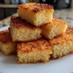 A stack of golden-brown, perfectly cut squares of crispy rice dessert on a white plate.