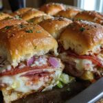 Close-up of baked grinder sliders filled with melted cheese, salami, and red onion on a baking sheet.