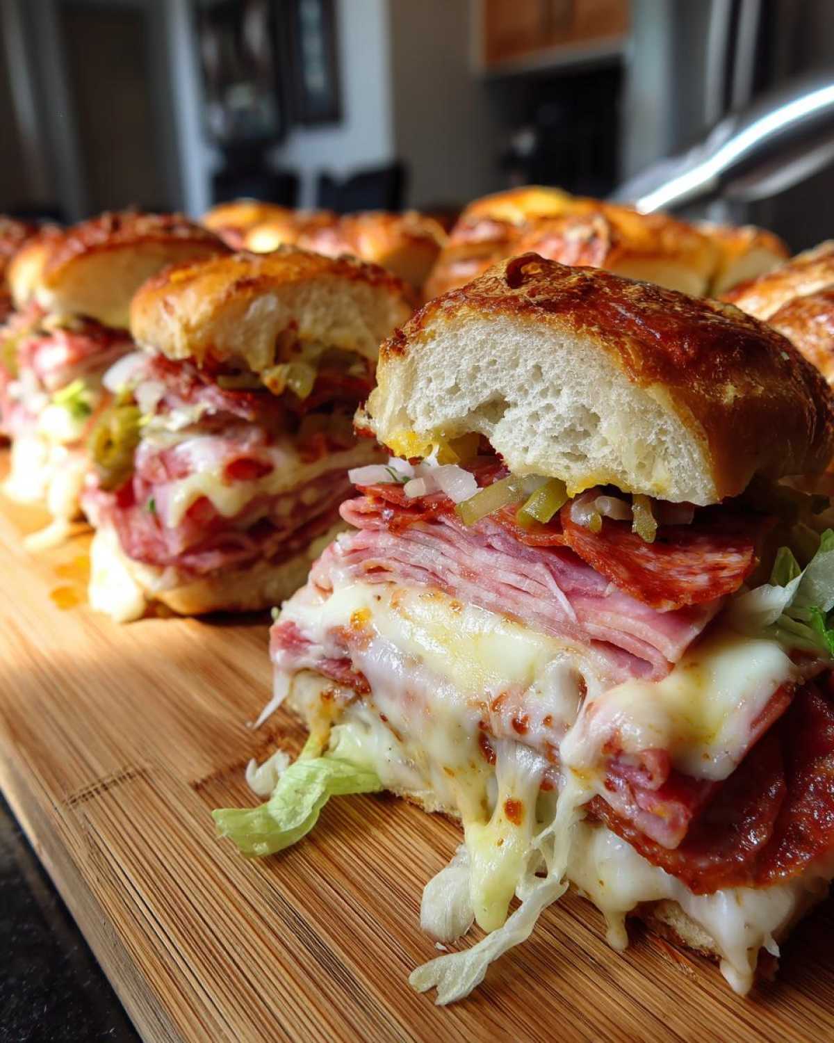 Close-up of cheesy, stacked meat grinder sliders on a wooden board with melted cheese dripping.