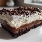 A decadent slice of layered chocolate mud pie featuring a dark crust, two chocolate fillings, whipped cream, and chocolate shavings.