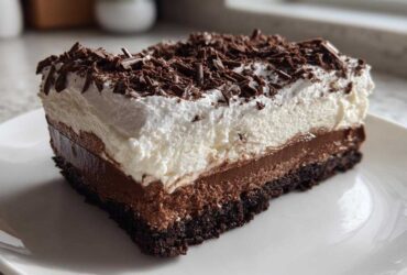 A decadent slice of layered chocolate mud pie featuring a dark crust, two chocolate fillings, whipped cream, and chocolate shavings.