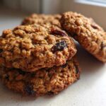 A close-up stack of three perfectly baked oatmeal raisin cookies on a light countertop.