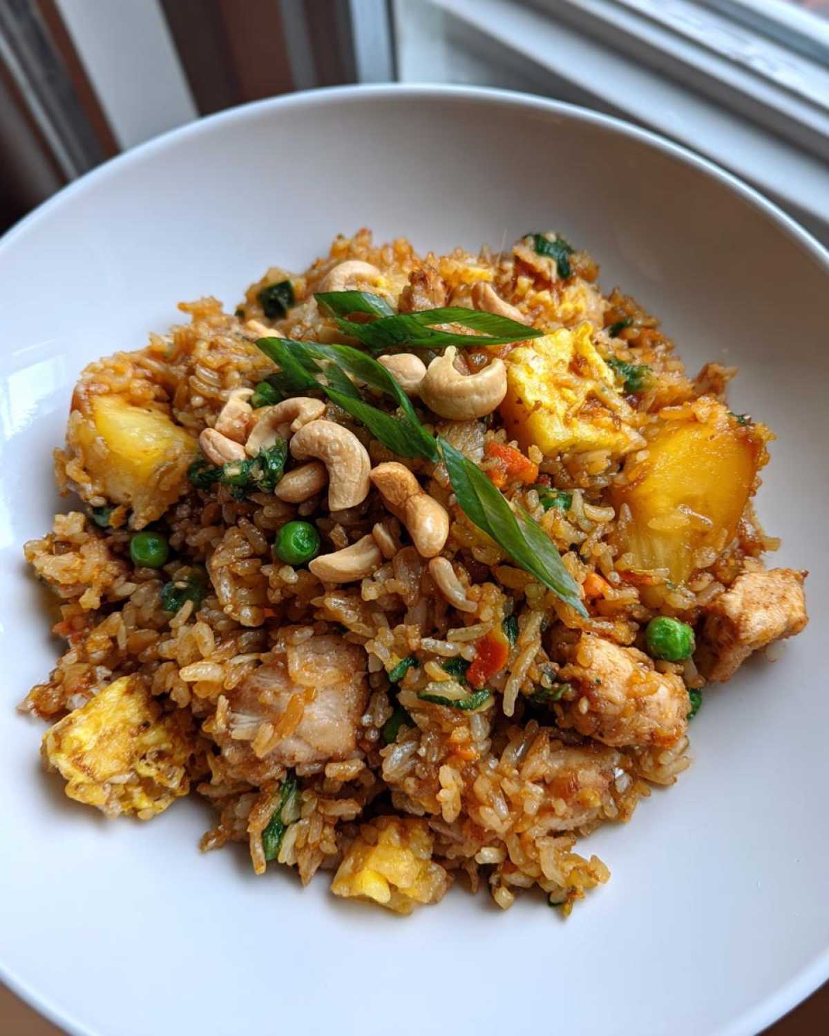 A close-up of a bowl filled with amazing pineapple fried rice, topped with cashews and green onions.