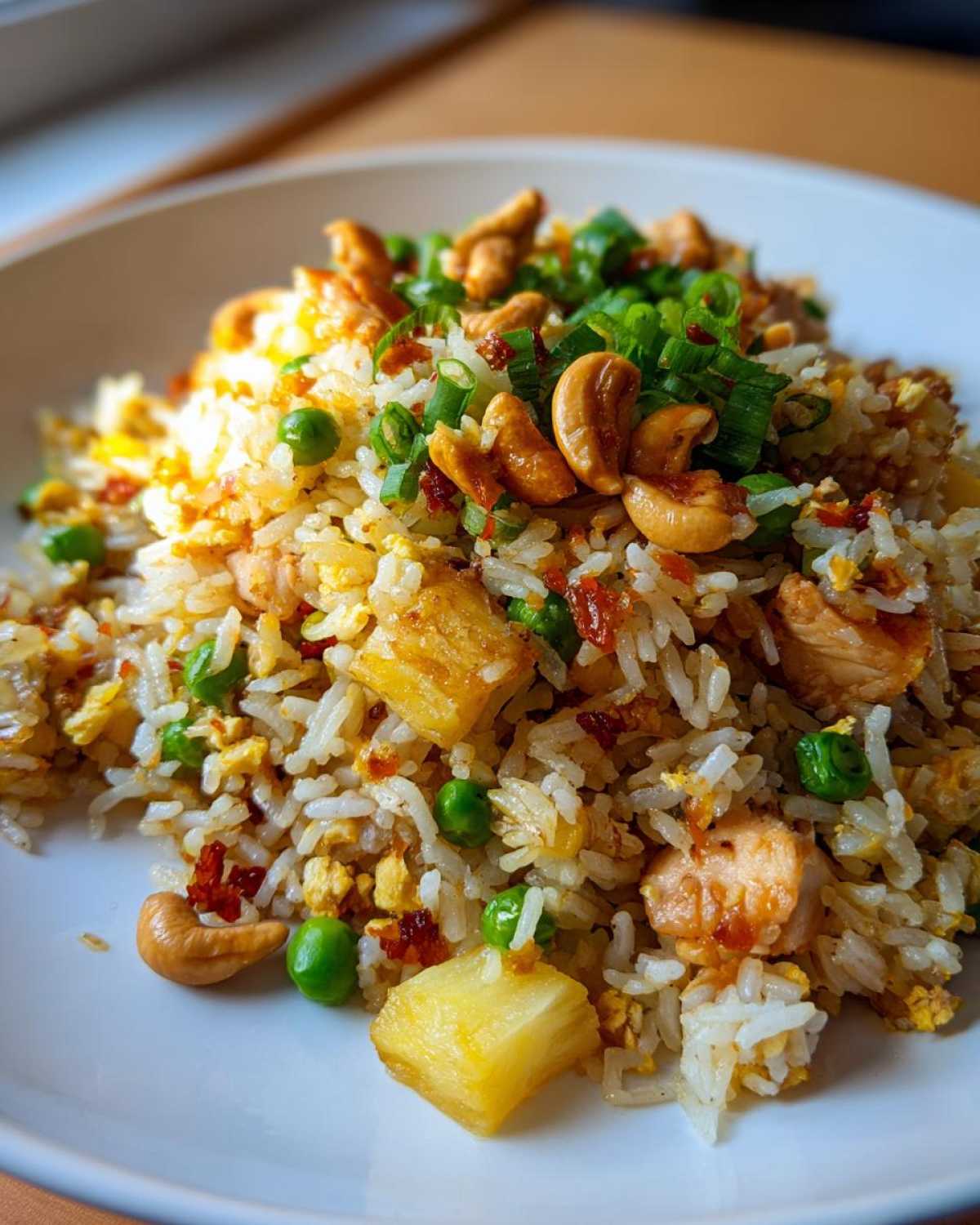 A close-up of a serving of vibrant pineapple fried rice, topped with cashews and green onions.