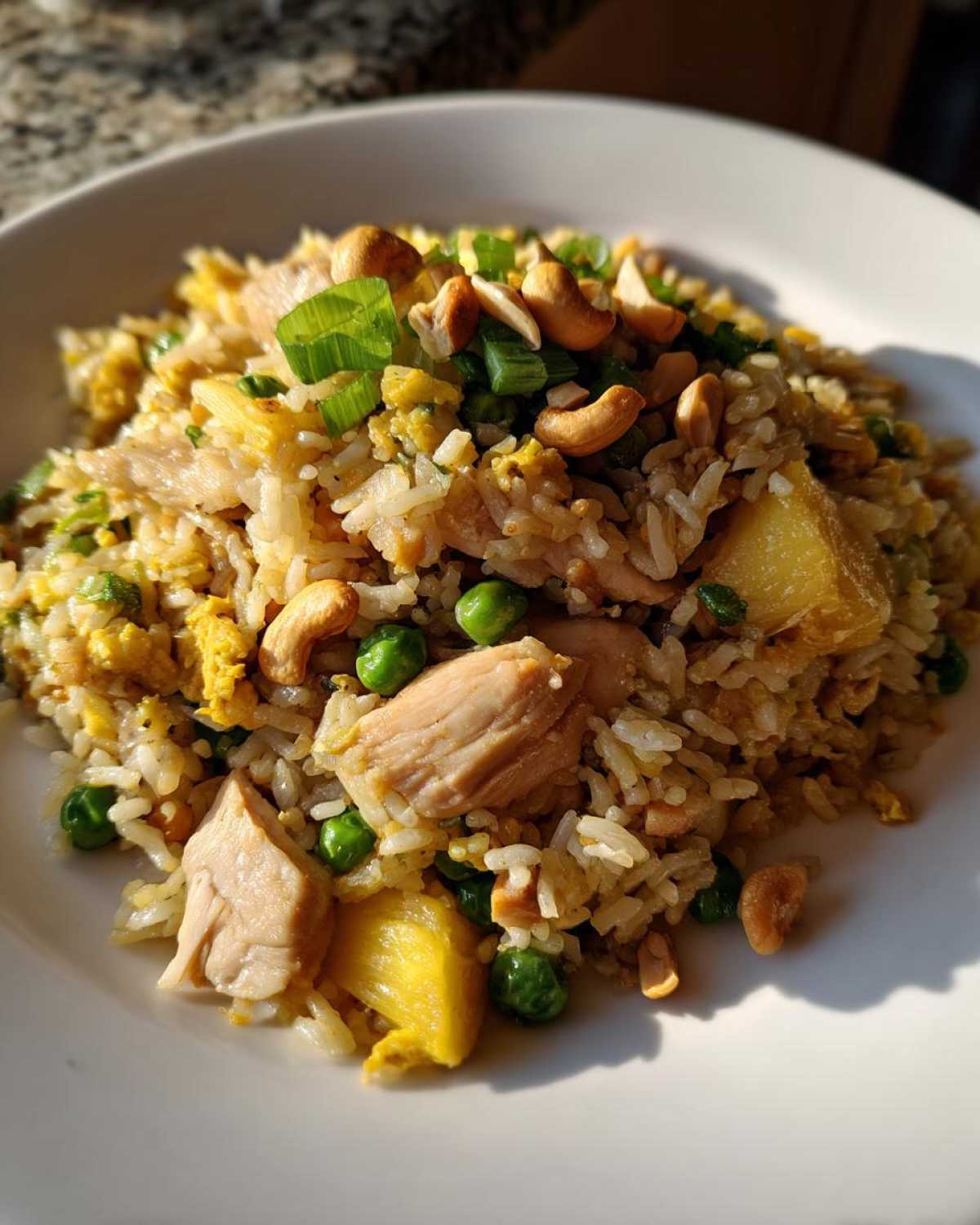 Close-up of a serving of amazing pineapple fried rice mixed with chicken, peas, egg, and topped with cashews and green onions.