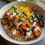 A close-up of a vibrant shrimp bowl featuring grilled shrimp over brown rice, topped with corn, black beans, avocado, and a creamy sauce.