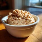 A close-up of a creamy, textured tuna dip served in a small white bowl on a sunlit wooden table.