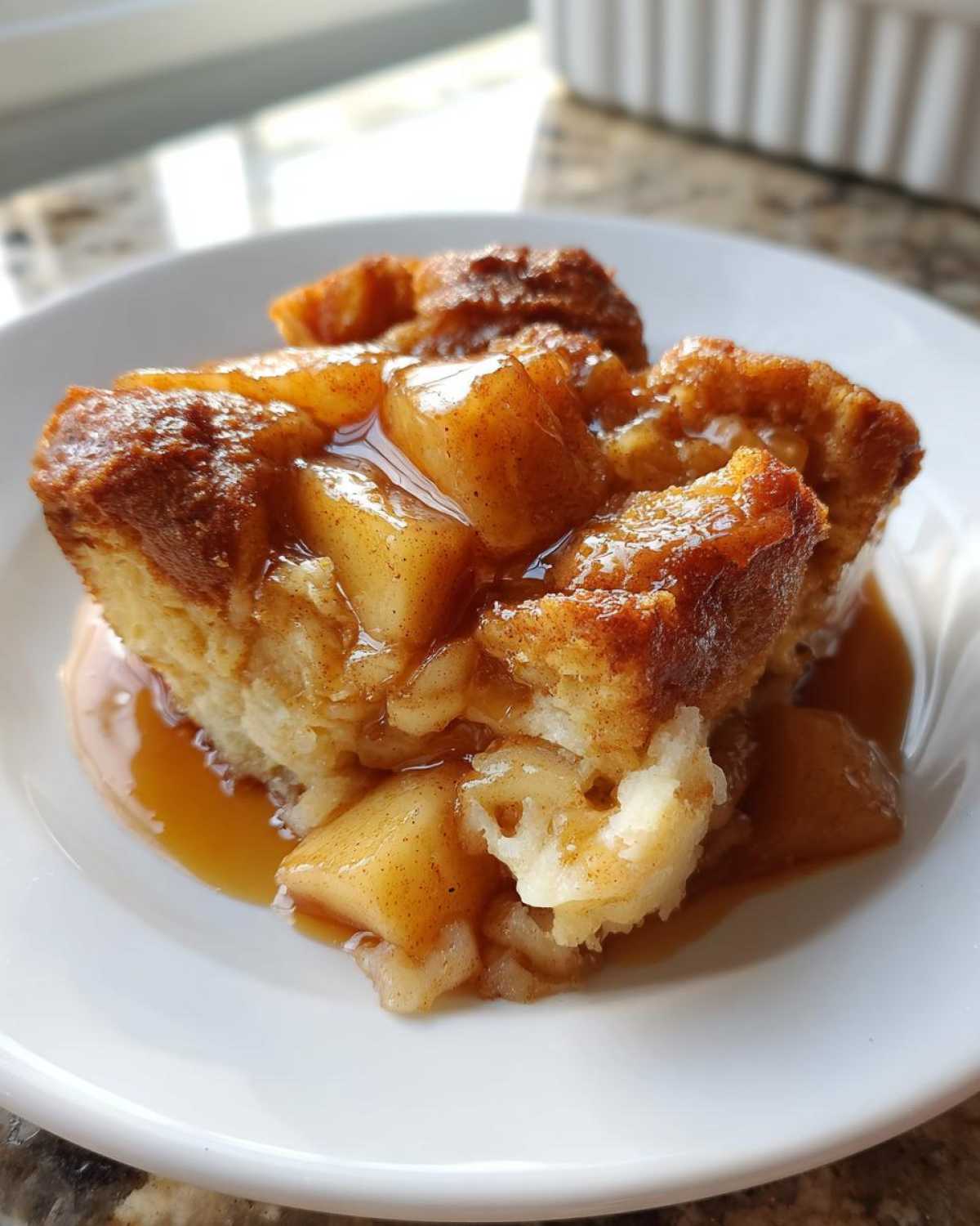 A close-up of a serving of apple bubble up casserole, featuring cinnamon-coated apple chunks and sweet glaze on a white plate.