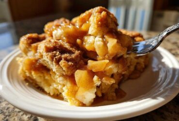 A fork lifts a bite of warm apple bubble up casserole covered in gooey cinnamon caramel sauce.