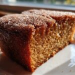 Close-up of a moist slice of Apple Cider Donut Cake, featuring a rich brown crumb and a sparkling cinnamon-sugar topping.