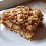 Close-up of a square slice of apple crisp cake showing layers of soft apples and a crunchy oat topping.