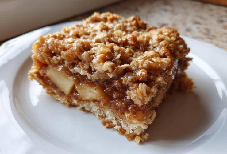 Close-up of a square slice of apple crisp cake showing layers of soft apples and a crunchy oat topping.