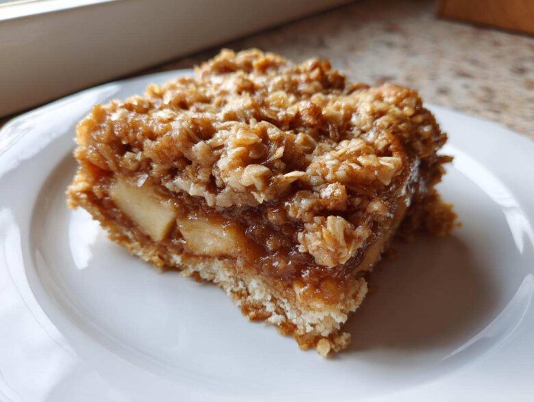 Close-up of a square slice of apple crisp cake showing layers of soft apples and a crunchy oat topping.