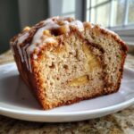 A close-up view of a slice of moist apple fritter bread topped with a sweet vanilla glaze.