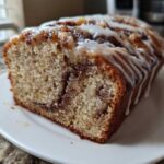 A close-up of a moist slice of apple fritter bread with a cinnamon swirl and white glaze drizzled on top.