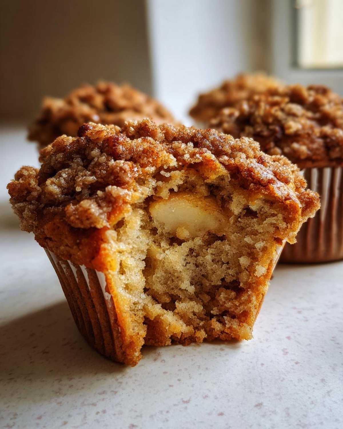 A bite taken out of an Apple oatmeal muffin showing soft interior and large apple chunks under a sugary brown crumb topping.