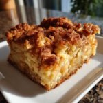Close-up of a square slice of apple pie dump cake featuring soft apple filling and a golden, cinnamon-sugar crumb topping.