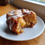 A single baked apple fritters, broken open to show soft interior and chunks of apple, drizzled with white glaze.